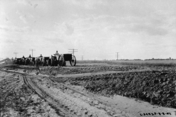 View across tire tracks in the dirt towards a group of men driving industrial tractor pulling wagons at a road construction site.