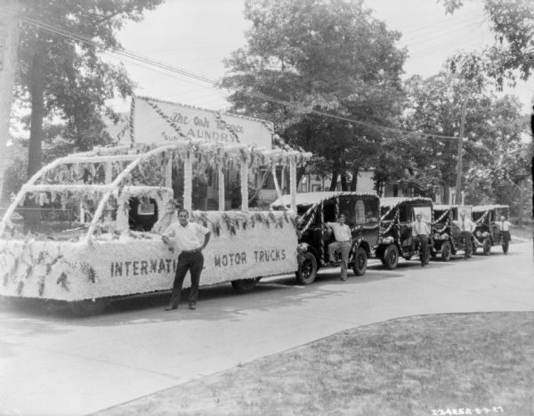 View down street towards men posing with a fleet of trucks for The Oak Terrace Laundry decorated for a parade.