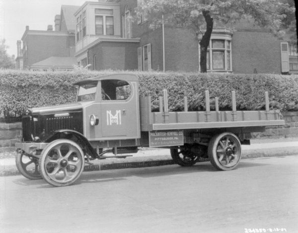 View across street towards a the driver's side of a delivery truck parked along a curb. A sign on the truck bed reads: "Macinosh-Hemphill Co. Best in Rolling Mill Machinery."