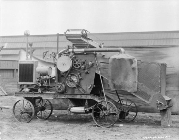 Threshing machine outdoors. In the background is a backdrop and an industrial building.