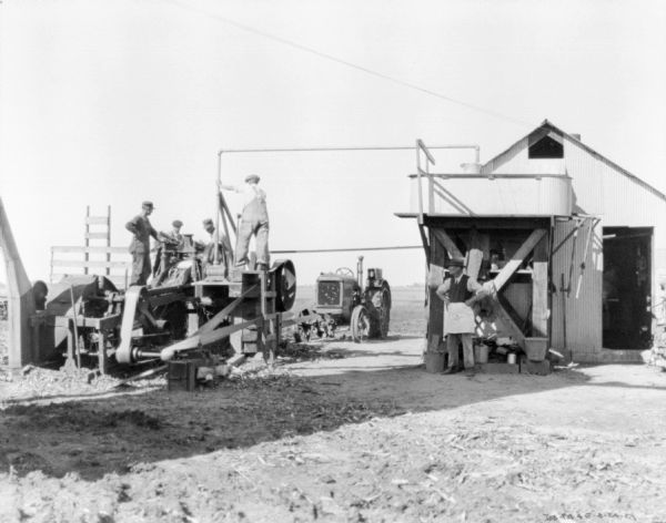 Group of men working with a Farmall tractor powering machinery.