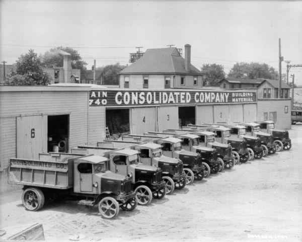 Elevated view of fleet of trucks parked in a row in front of a Consolidated Co. building.