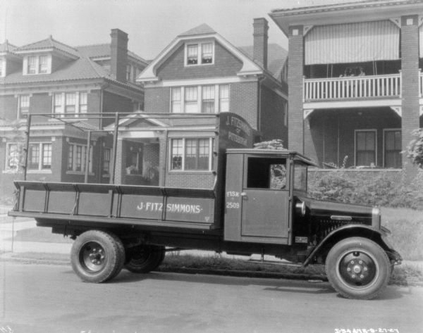 View across street towards a truck parked along the opposite curb in front of a row of three large houses. The sign painted on the front of the truck bed reads: "J. Fitzsimmons of Pittsburgh."