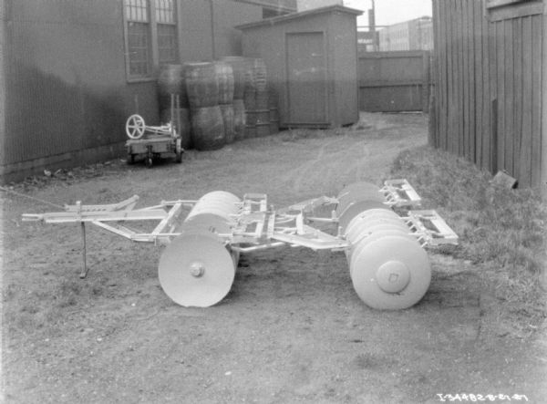 Disk harrow set up outdoors in a yard near buildings.