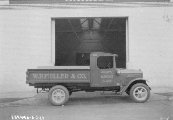 Passenger side view of a truck parked in front of an open garage door. The signs painted on the side of the truck read: "W.P. Fuller & Co." and "Paints Varnishes Glass."