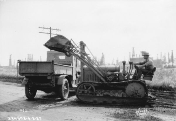 Man operating an earthmover and dumping material into a dump truck.