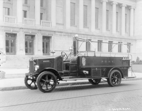 View across street towards a fire truck parked along a curb. A large building is in the background. The sign painted on the side of the truck reads: "F.D.N.Y."