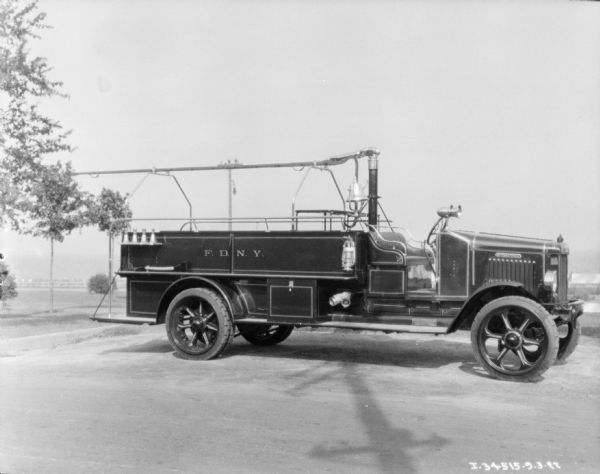 View towards a Model 54-C 1927 fire truck parked along a curb. The sign painted on the side of the truck reads: "F.D.N.Y."