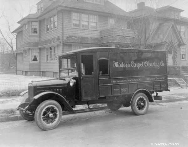 View across street towards a truck parked along the opposite curb. The sign painted on the side of the truck reads: "Modern Carpet Cleaning Co." Houses are along a sidewalk in the background.