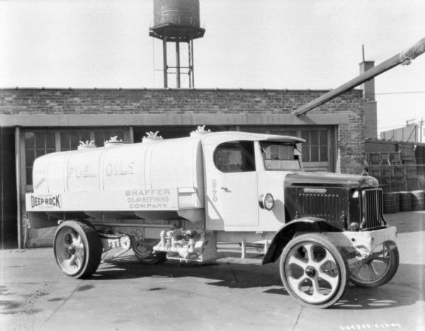 Right side view of a gasoline delivery truck parked in front of a brick building. The sign painted on the truck reads: "Fuel Oils, Deep-Rock, Shaffer Oil and Refining Company." Behind the building is the top of a water tower. 