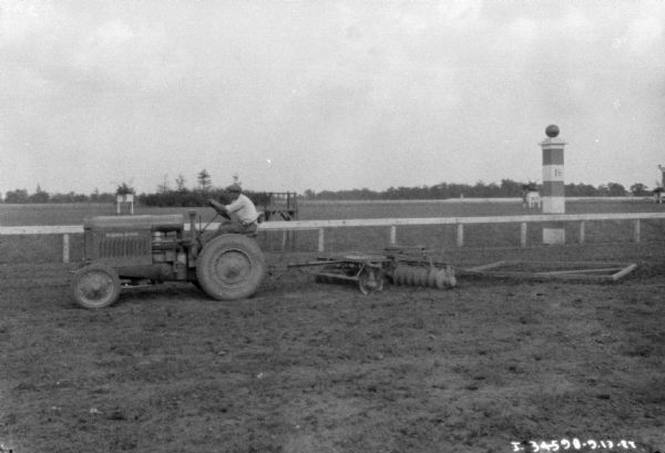 View of a man smoothing a race track with a tractor pulling a disk harrow.