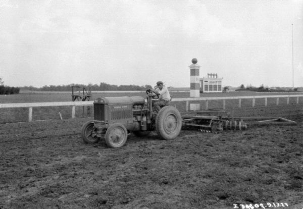 View of a man smoothing a race track with a tractor pulling a disk harrow.