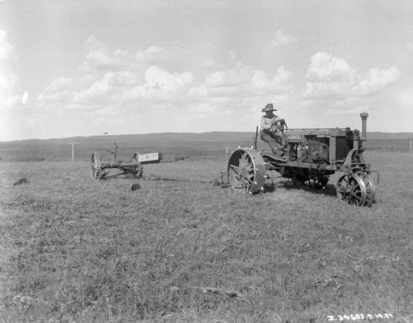 View across field towards a man using a Farmall to pull a mower.