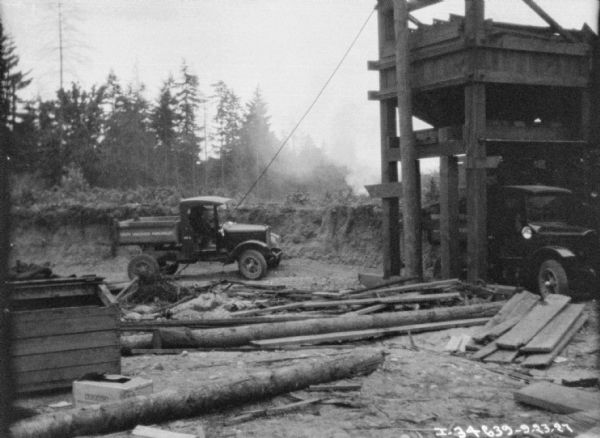 Delivery trucks at a construction site. On the right is a tall, wood building for loading material into the back of the trucks.