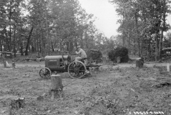 A man is removing a stump with a Farmall tractor at Morris Bros. Ranch. Downed trees are in the background.