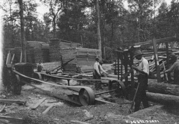 Men are working at a sawmill at the C.W. O'Halloran Co. There is a tractor in the background that is being used to belt-drive machinery.
