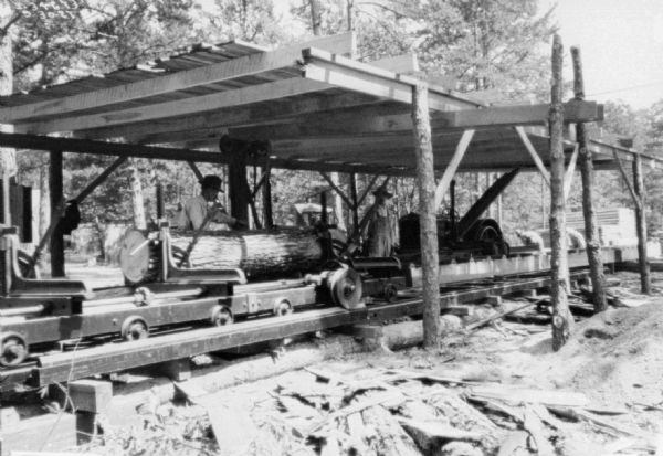 Men are working at a sawmill at the C.W. O'Halloran Co. There is a tractor in the background that is being used to belt-drive machinery.