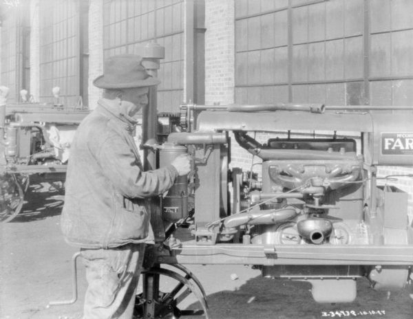 A man is holding a tool against a Farmall tractor engine while standing outdoors in front of a brick building at a dealership.