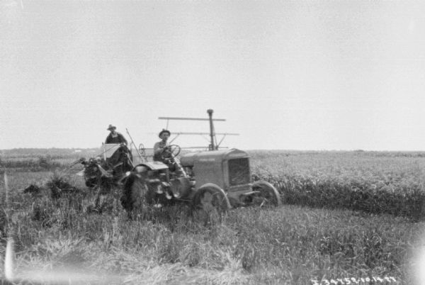 View of a man driving a McCormick-Deering tractor pulling a man on a harvester-thresher in a field.