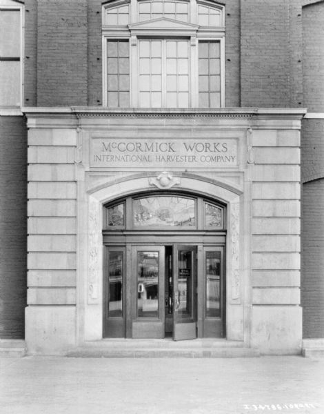 View towards the entrance to a dealership. A sign on the double door reads: "Office Entrance." There are stained glass windows in the transom above the door which depicts a harvester-thresher working in a field.