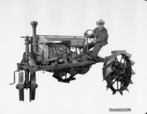 Three-quarter view from front left of a man driving a Farmall tractor.