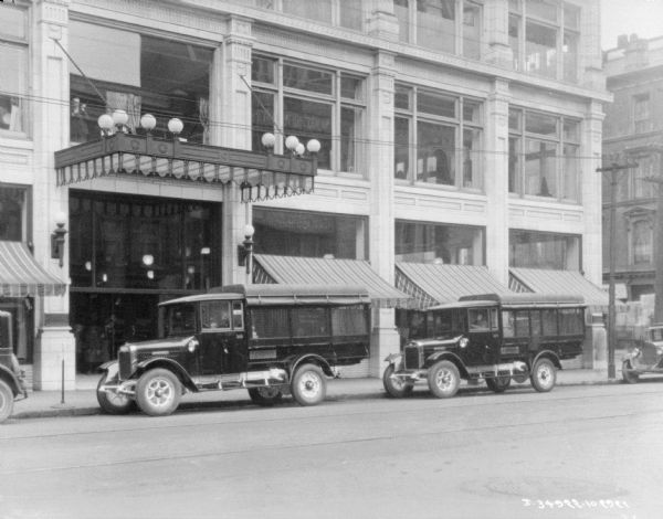 View across street towards two delivery trucks parked along the opposite curb in front of storefronts.