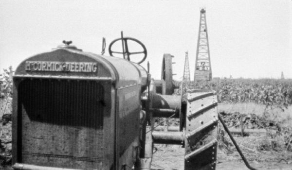 Close-up of front of tractor at worksite. Oil rigs are in the background.