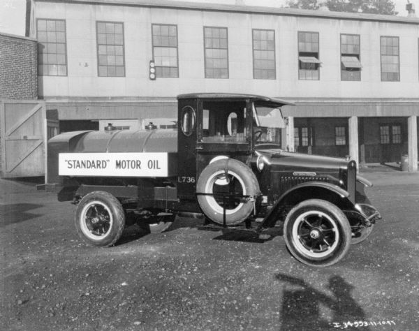 Passenger side view of a "Standard" Motor Oil truck. In the background is a commercial building.