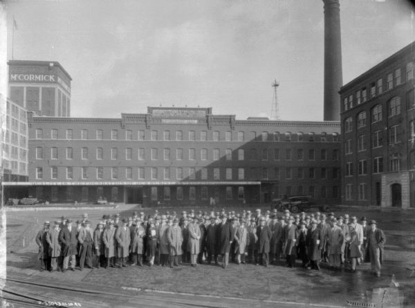 Elevated view of men and women standing together for a group portrait in the yard at McCormick Works. The sign above the loading dock reads: "Quality is the Foundation of Our Business."