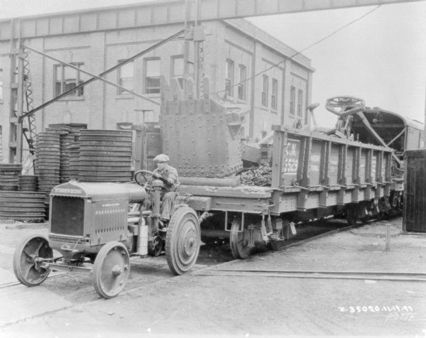 A man is driving an industrial tractor to pull a railroad car on railroad tracks.