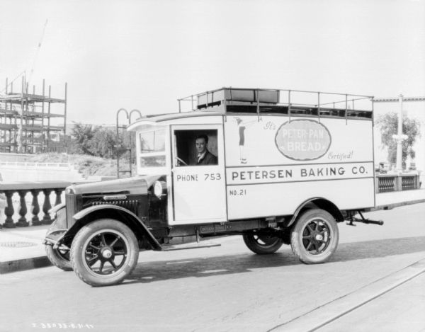View of a man sitting in the driver's seat of a truck parked on a bridge. The sign painted on the truck reads: "Peterson Baking Co."