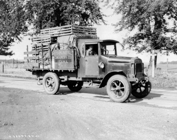 View towards a man sitting in the passenger seat of a truck. The bed of the truck is loaded with crates.