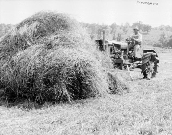 A man is using a tractor to move a pile of hay in a field.