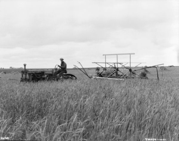 View across field towards a man driving a Farmall tractor pulling a harvester-thresher in a field.