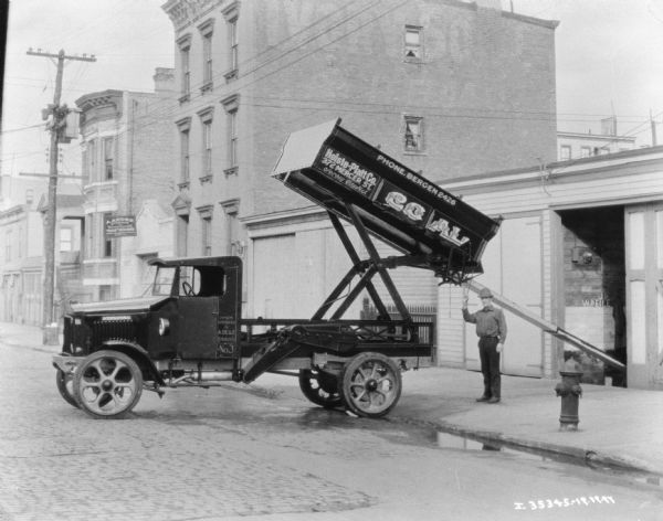 View down street towards a man using a truck to dump coal into a chute. The sign on the truck reads: "Holste-Platt Co."