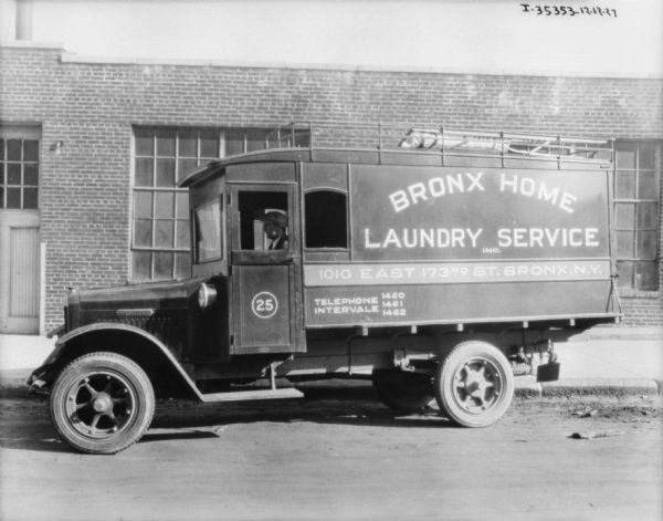 View across street towards a man sitting in the driver's seat of a laundry delivery truck. The sign on the side of the truck reads: "Bronx Home Laundry Service Inc."