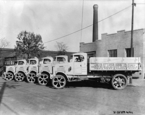 Five men are sitting in the driver's seats of five trucks, parked in an angled line near a building. The sign on the truck in the front reads: "Hugh O'Haire Co. Inc. Mason's Building Materials."