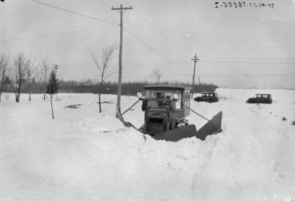 View towards front of truck with a snowplow. The plow is moving through deep snow in a rural area.