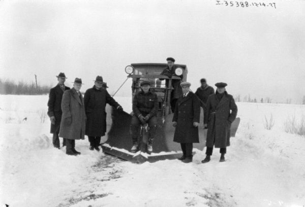 A group of men are posing around a truck with a snowplow mounted on the front. There is deep snow on the ground.