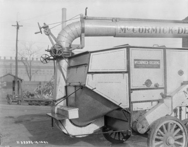 View of a section of a McCormick-Deering thresher parked outdoors in a factory yard.