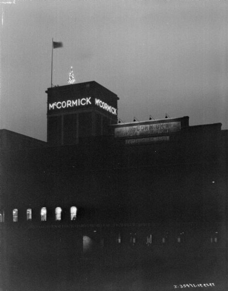 View looking up at McCormick Works at night, with a Christmas tree on the roof near the flag pole, and the "McCormick" sign lit up.
