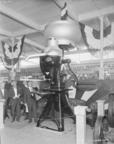 A group of men are standing on the left looking up at a giant cream separator on display in an exhibition hall.