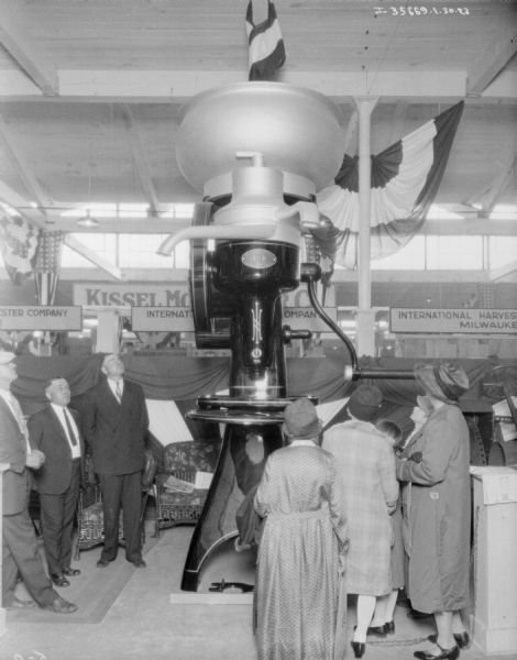 A group of men and women are looking at a giant cream separator on display in an exhibition hall.