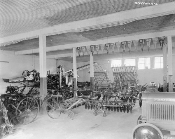Slightly elevated view of agricultural machinery on the floor of a dealership. The front of a McCormick-Deering tractor is on the right.