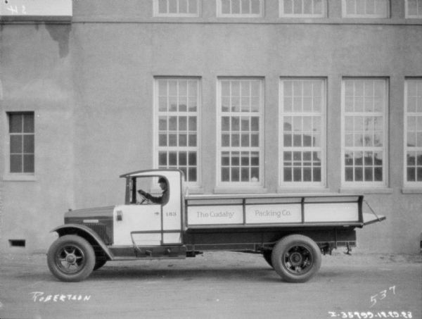 View across street towards a man sitting in the driver's seat of a delivery truck parked in front of a building. The sign painted on the truck bed reads: "The Cudahy Packing Co."