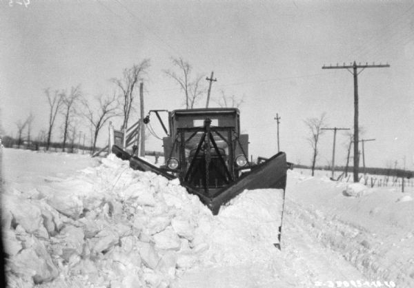 View of front of truck with a snowplow plowing a road.