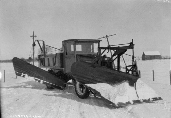 A snowplow on a truck parked on a plowed road in a rural area.