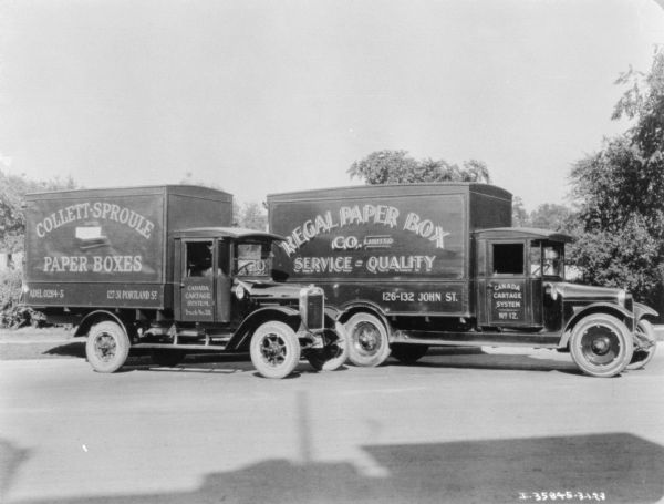 Two delivery trucks parked together. The signs painted on the side of the trucks reads: "Regal Paper Box Co. United, Service — Quality," and "Canada Cartage System."