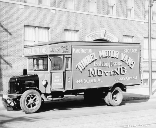 View across street towards a truck parked along the curb. The sign reads, in part: "Local & Long Distance Moving," "Piano Hoisting" and "Storage."