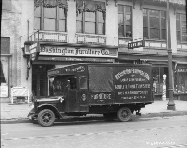 View across street towards men sitting in a delivery truck parked along the curb. The Washington Furniture Co. storefront is in the background.